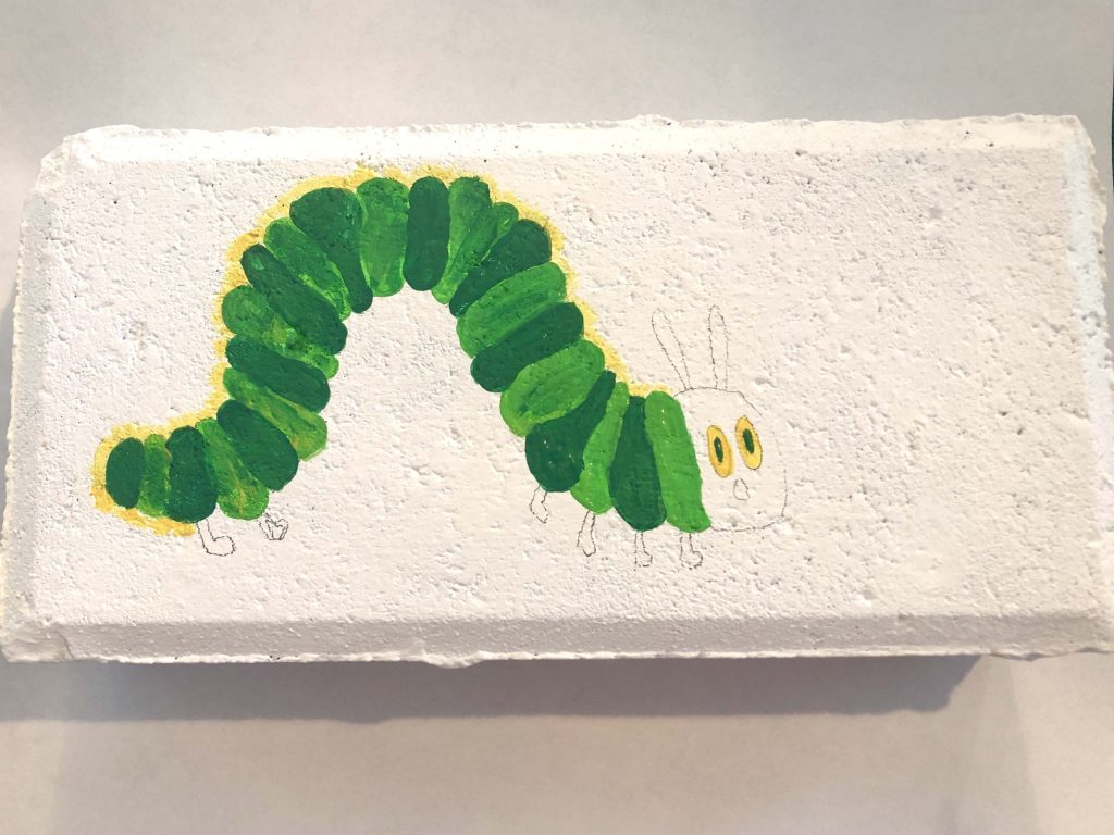 A brick with a half-painted design of a caterpillar.